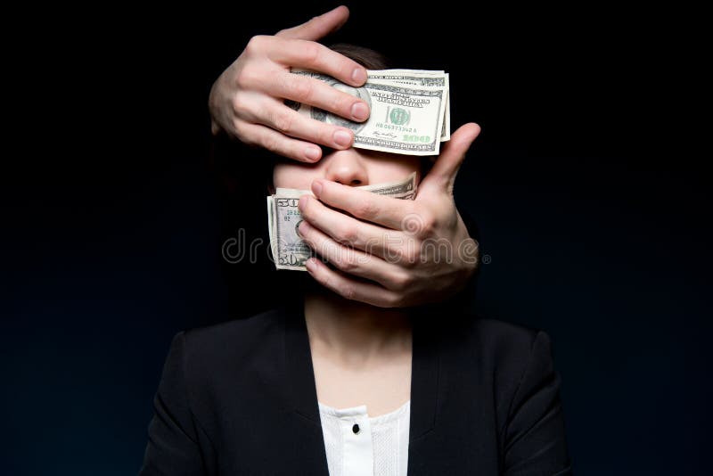 Hands out of the darkness cover the eyes of a business woman with money