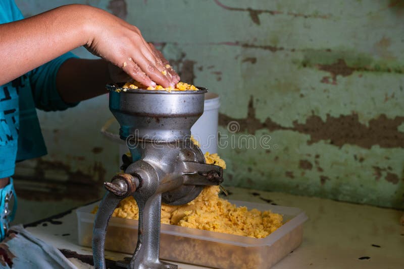 Hands Putting the Cooked Corn in the Grinding Machine for the