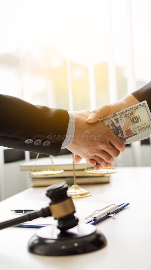 Hands sending money under corrupt bribery Close-up of two businessmen shaking hands and taking bribes under a wooden table in the office. Hands sending money under corrupt bribery Close-up of two businessmen shaking hands and taking bribes under a wooden table in the office..