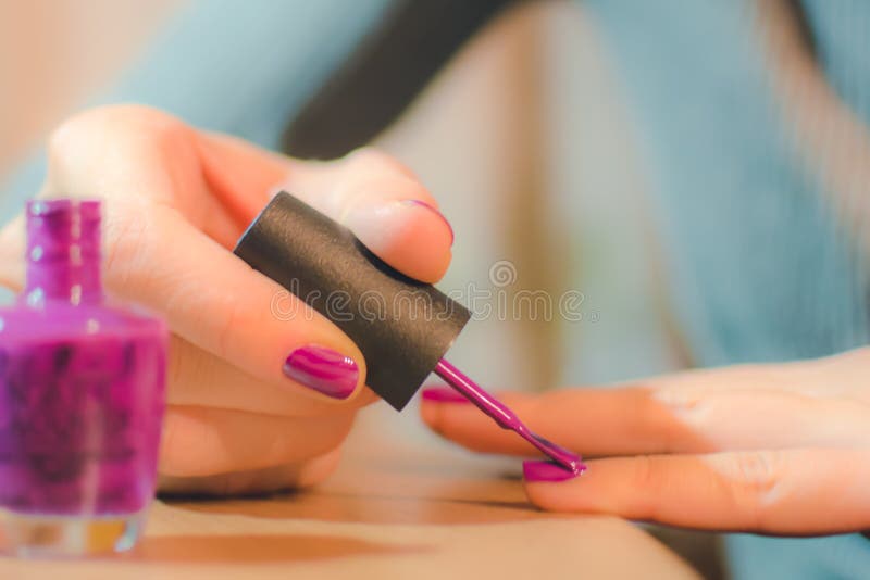 Hands of the woman painting nails bright varnish