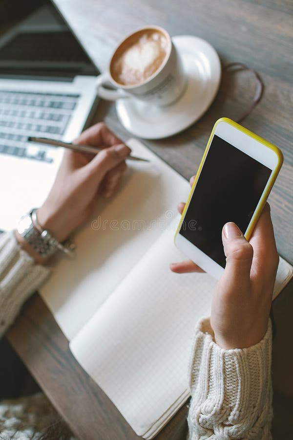 Hands of woman with pen and notepad, holding smartphone with coffee