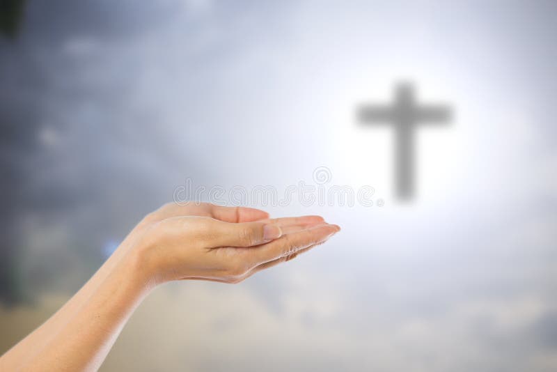 Hands of women praying over blurred the cross on the sky backgro