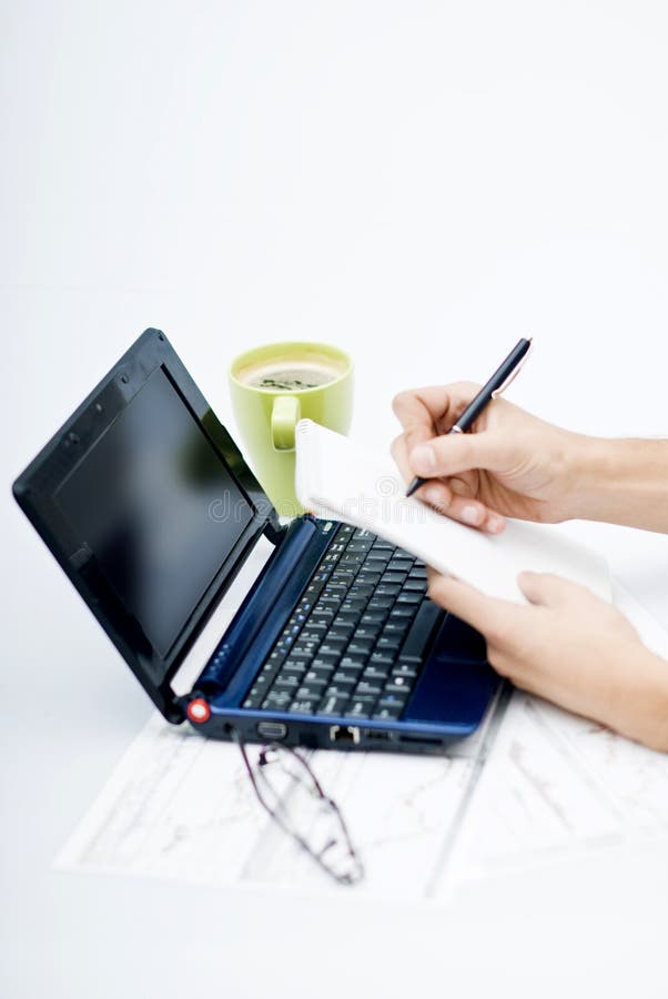 Hands writing in agenda with laptop in front