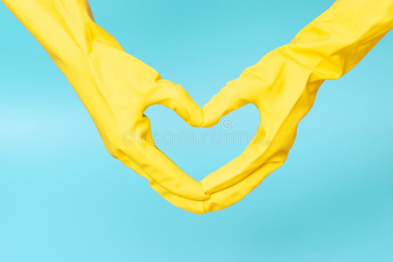 Hands in yellow rubber gloves in the shape of a heart on blue background. Hands in yellow rubber gloves in the shape of a heart on a blue background stock photo