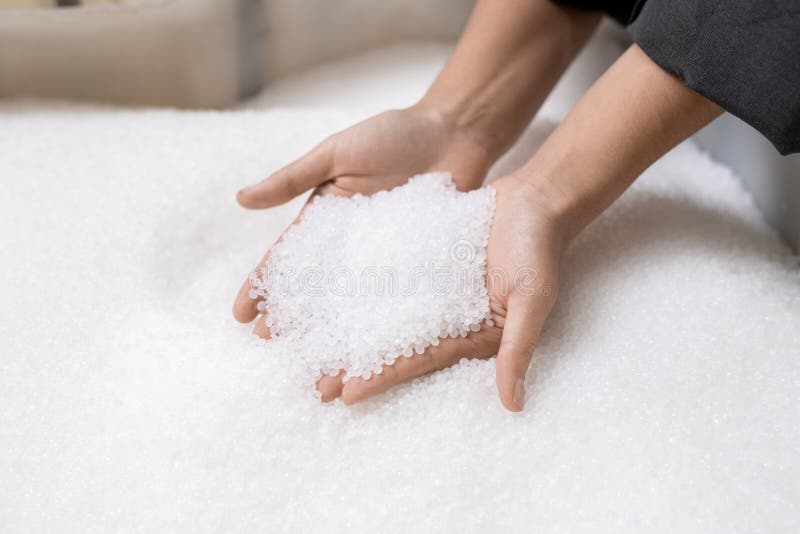 Hands of young female worker holding pile of unprocessed white plastic pellets