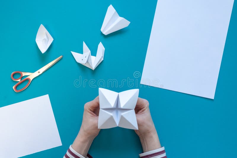 Hands of a young girl make paper art of origami, on a blue background stock images Hands of a young girl make paper art of origami, on a blue background stock images