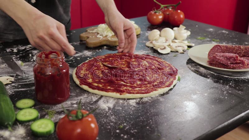 Hands of young girl smear tomato paste on pizza dough