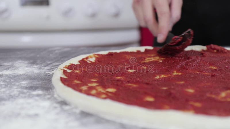 Hands of a young man put and smear tomato paste on pizza dough close up