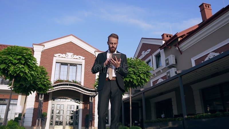 Handseher Bartkasier, der in einem klassischen Anzug mit Krawatte gekleidet ist, benutzt einen Tablet-Computer, wenn er in der Nä