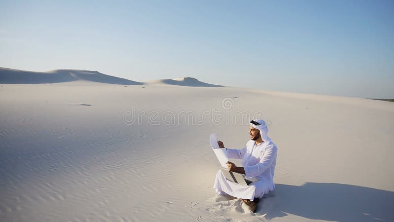 Muslim Arabian UAE Sheikh architect sitting with laptop on sand