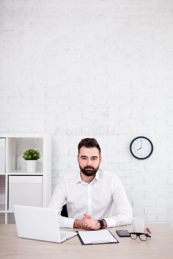 Handsome bearded businessman sitting in office - copy space over white brick wall stock photo Handsome bearded businessman sitting in office - copy space over white brick wall stock photo