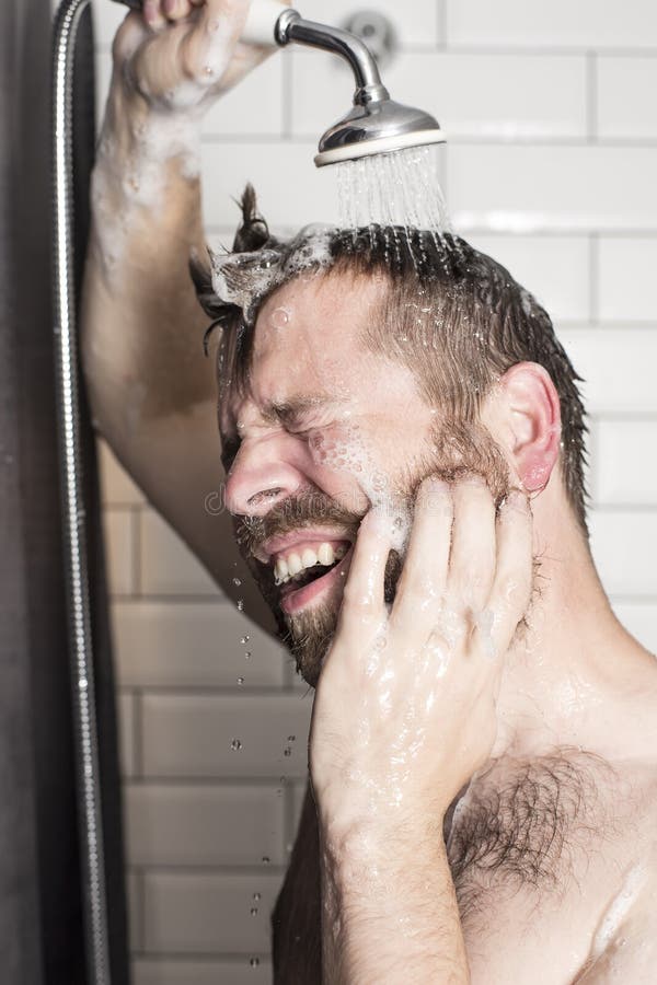 A handsome, bearded man washes the shampoo from his hair in the stock image A handsome, bearded man washes the shampoo from his hair in the stock image