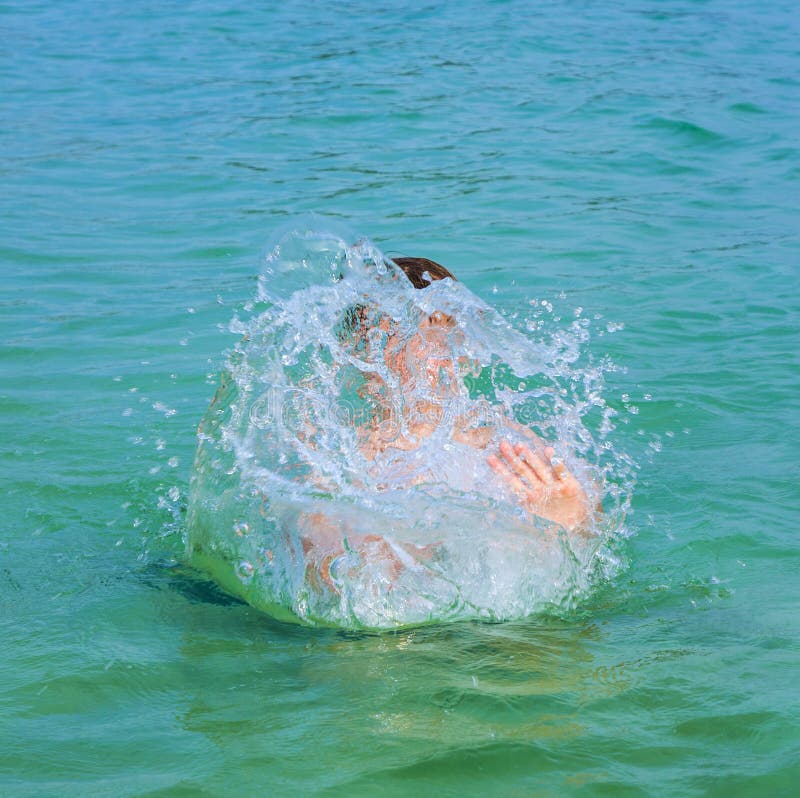 handsome boy enjoys sputtering with his hand in the tropical ocean