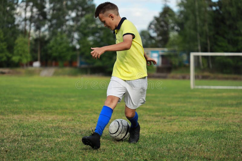 Handsome boy soccer player in a yellow t-shirt on the soccer field plays with a ball