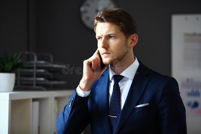 Handsome businessman in suit speaking on the phone in office