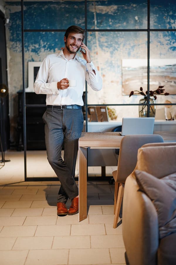 Handsome businessman in suit standing and talking on smartphone in modern office.