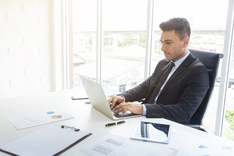Handsome businessman working at desk with laptop and paper graph in office. Professional businessman and technology concept royalty free stock photos Handsome businessman working at desk with laptop and paper graph in office. Professional businessman and technology concept royalty free stock photos