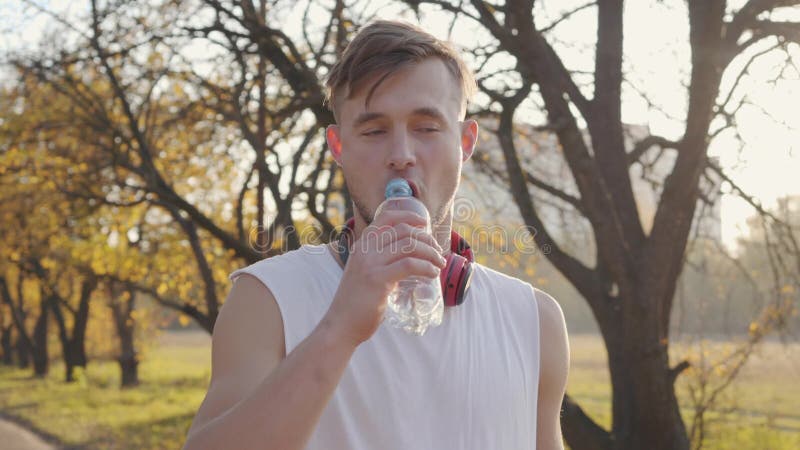 Handsome Caucasian athletic man in white singlet som står i solljus och dricksvatten Utbildning för unga idrottsungdomar stock video