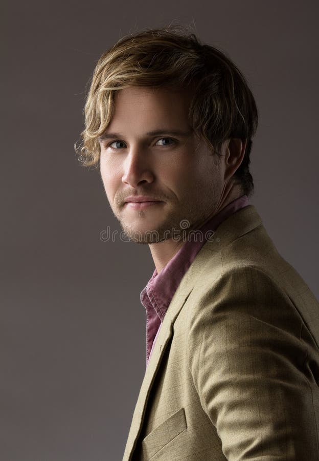 Portrait of a handsome blonde caucasian man wearing a pale purple button shirt with olive beige formal suit jacket. The man is smiling. Portrait of a handsome blonde caucasian man wearing a pale purple button shirt with olive beige formal suit jacket. The man is smiling.