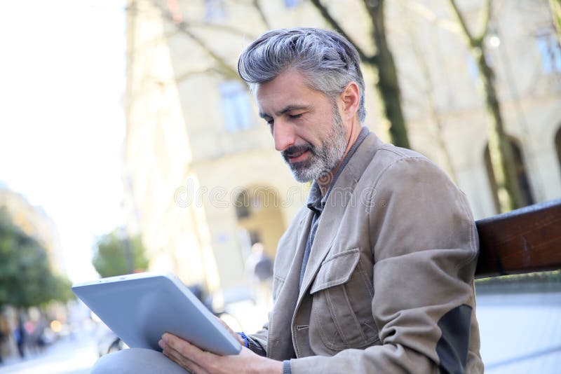 Handsome charming man websurfing on tablet in the streets