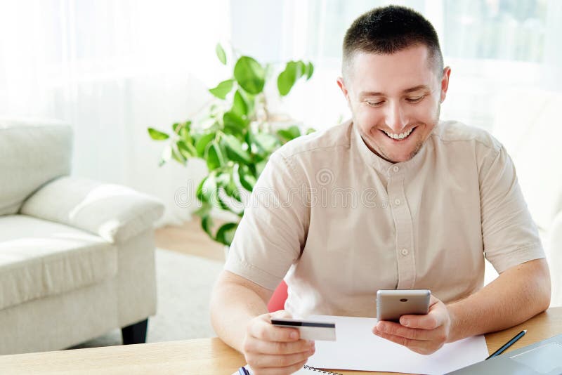 Handsome cheerful man paying with credit card on smart phone at home office, copy space. Technology, banking, business, online. royalty free stock photo Handsome cheerful man paying with credit card on smart phone at home office, copy space. Technology, banking, business, online. royalty free stock photo