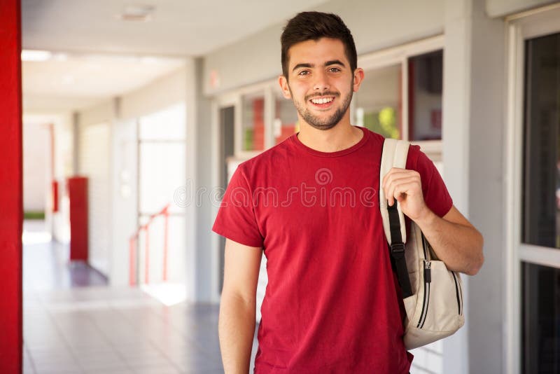 Ritratto di un Ispanico studente di college di portare uno zaino e in piedi in un corridoio della scuola.