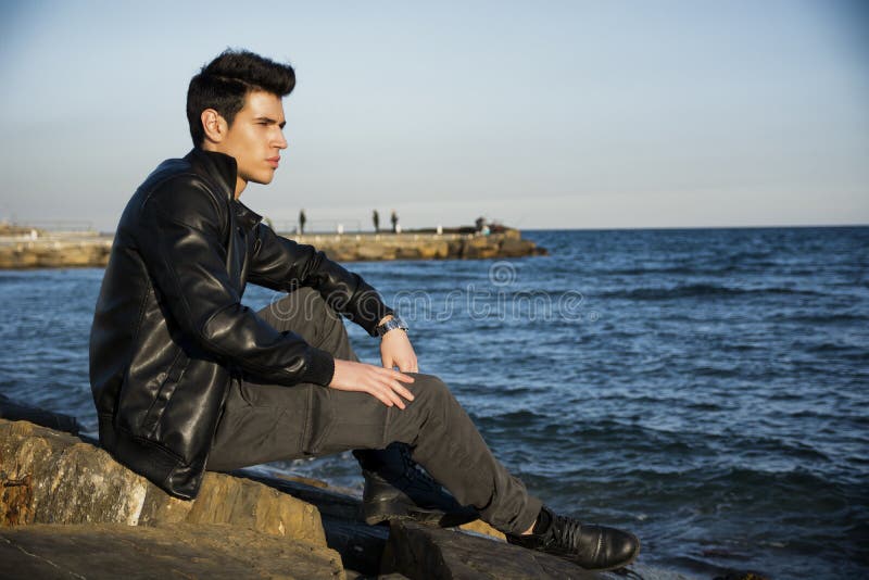 Handsome fashionable young man sitting at sea or