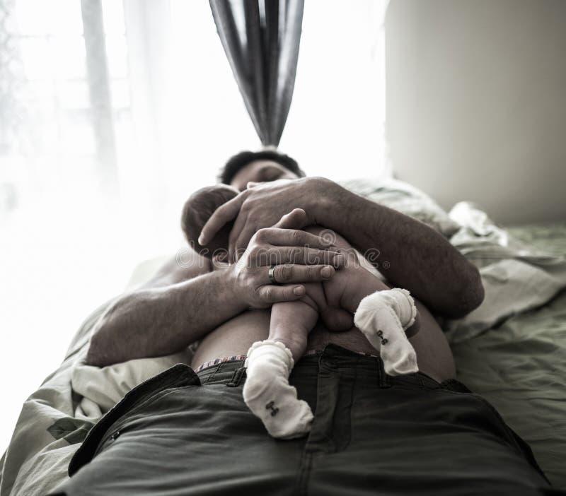 Handsome father is lying on the bed and holding with care his sweet new born baby son royalty free stock photography Handsome father is lying on the bed and holding with care his sweet new born baby son royalty free stock photography