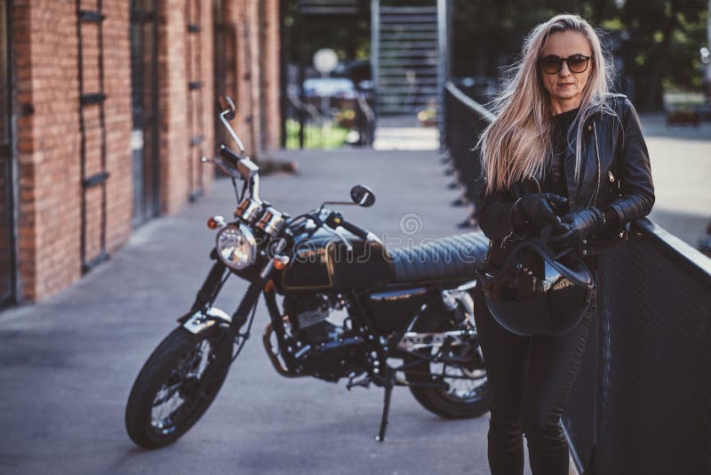 Handsome female biker is posing for photographer with her motorbike