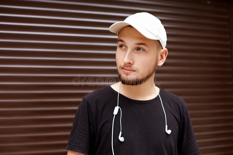 Handsome guy in a white cap and black t-shirt with headphones on the street