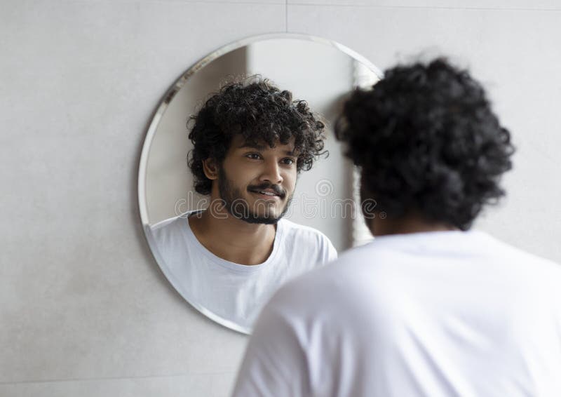 Handsome Indian Guy Looking at His Reflection in the Mirror, Standing