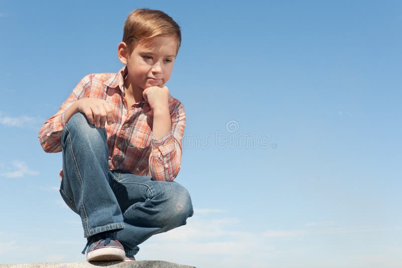 A serious boy is thinking about childish problems sitting against the sky. Boring kid white stock images, royalty-free photos and pictures