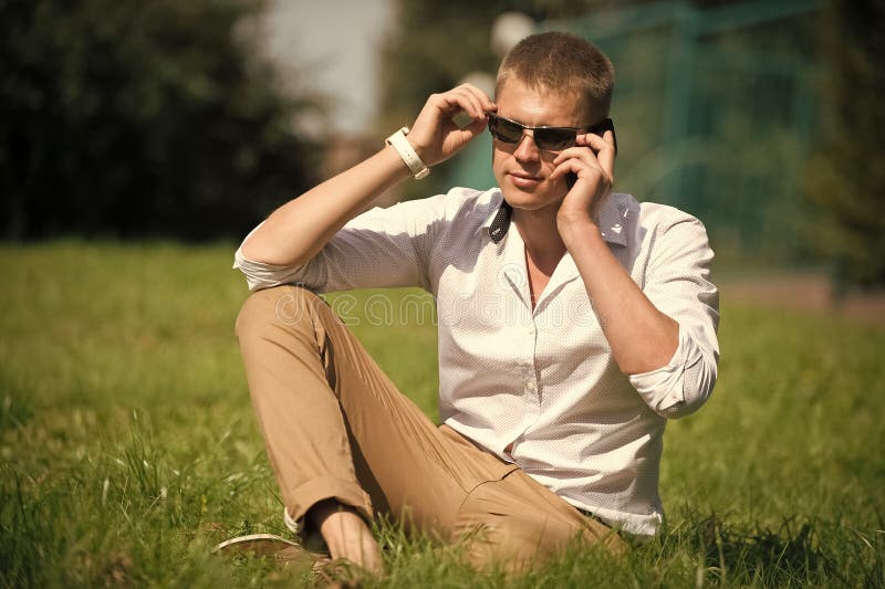 Handsome macho enjoy summer day. Businessman in sunglasses on sunny outdoor. Man relax on green grass. Fashion style and stock photos Handsome macho enjoy summer day. Businessman in sunglasses on sunny outdoor. Man relax on green grass. Fashion style and stock photos