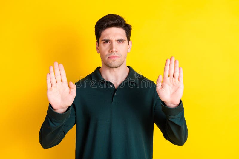 Handsome man in green polo expressing stop gesture with both hands on yellow background for advertising and promotions stock photos