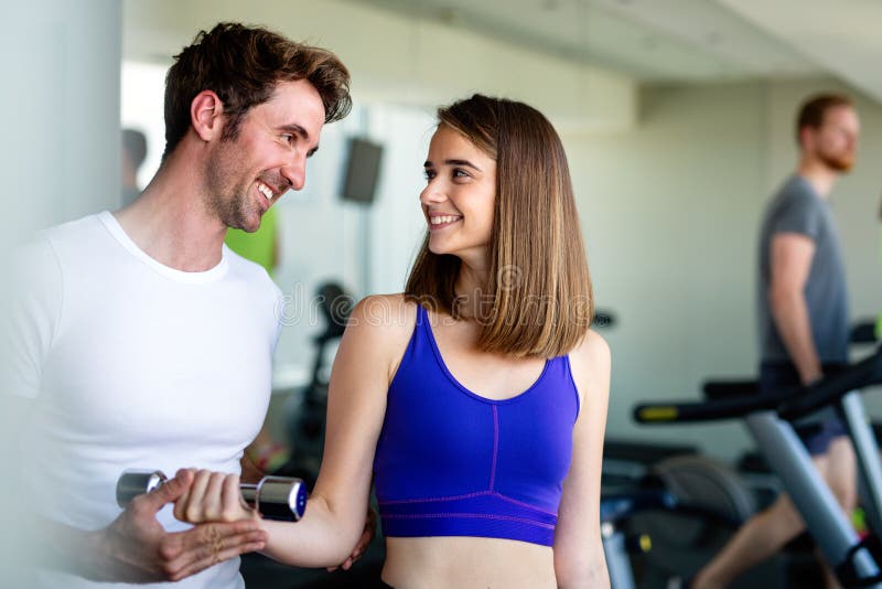 Handsome man personal trainer helping fit woman working with dumbbells in fitness gym club stock photo