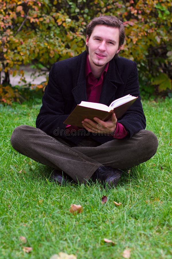 Handsome man reading book on a grass in autumn