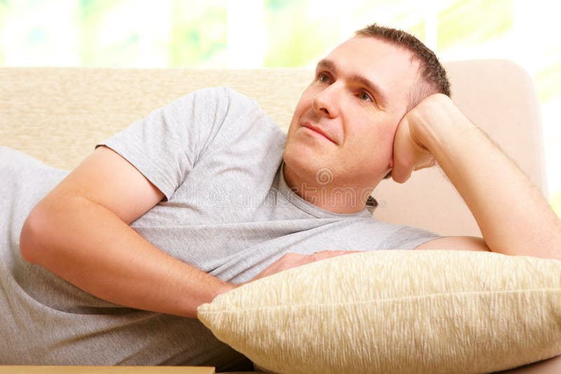 Handsome man resting on couch at home lost in though and gently smiling. Smiling asking stock images, royalty-free photos and pictures