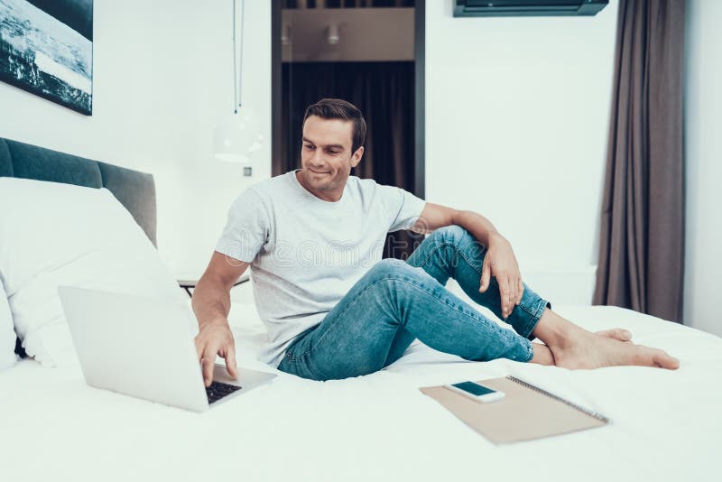 Handsome Man Sitting on Bed and Working on Laptop stock image Handsome Man Sitting on Bed and Working on Laptop stock image