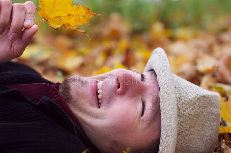 Handsome man smiling and lying in autumn leaves