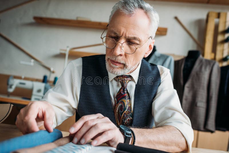 Handsome mature tailor looking at cloth samples royalty free stock photo