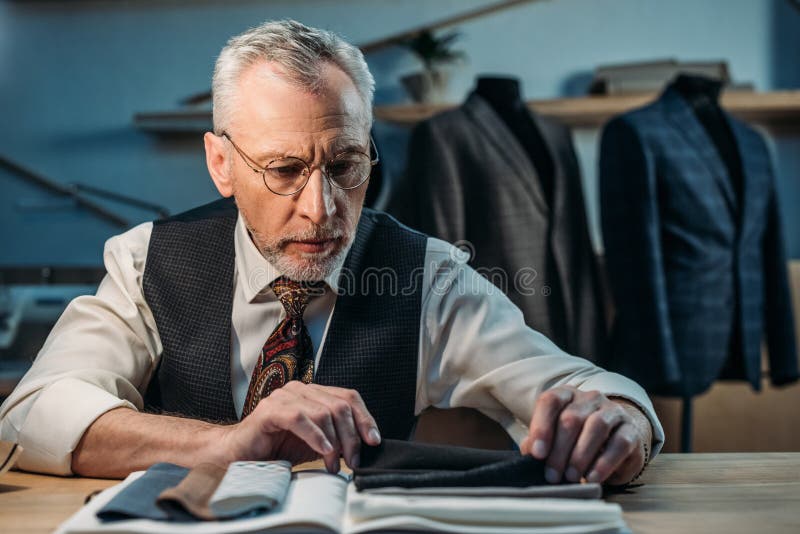 Handsome mature tailor working with cloth samples at sewing workshop royalty free stock images
