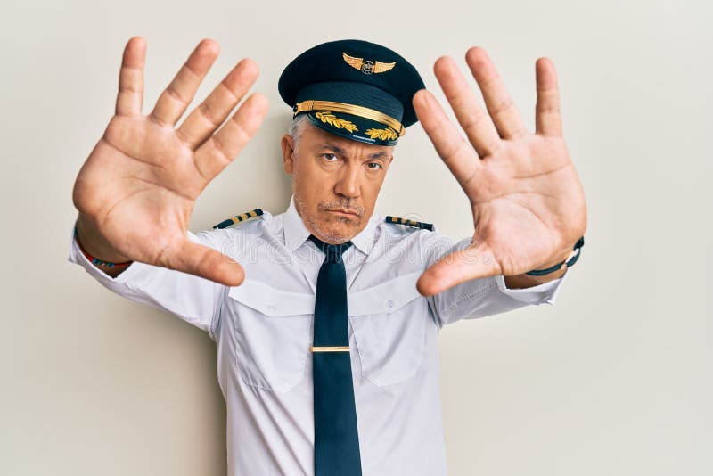 Handsome middle age mature man wearing airplane pilot uniform doing frame using hands palms and fingers, camera perspective stock images