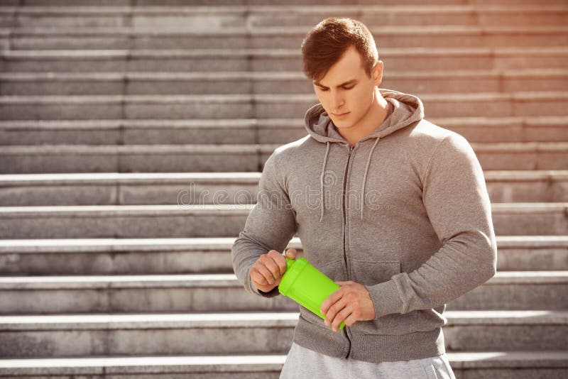 Handsome muscular man holding shaker, outdoors. Young active male drinking water.