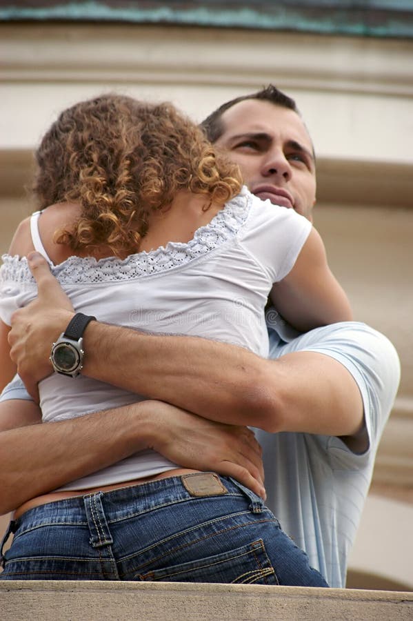 Handsome proud man with his arms wrapped around a lady hugging her close on balcony .shot on overcast day providing soft lighting. Handsome proud man with his arms wrapped around a lady hugging her close on balcony .shot on overcast day providing soft lighting