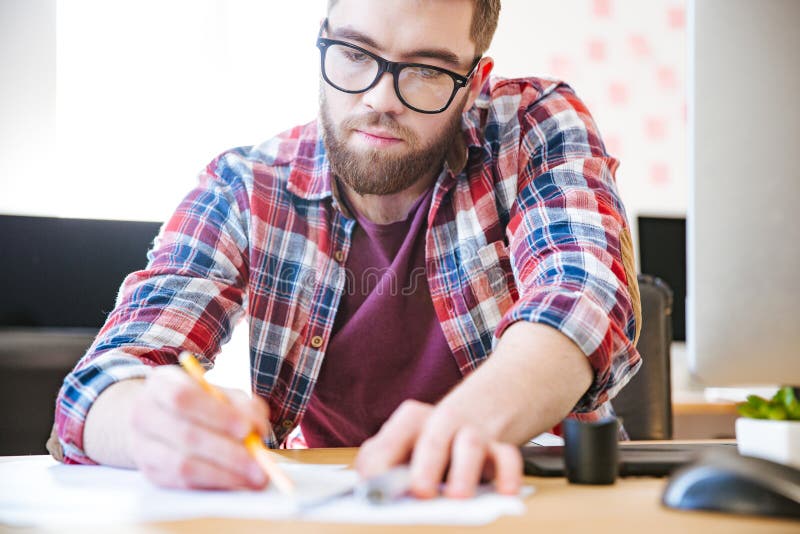 Handsome serious man sitting and writing in the office