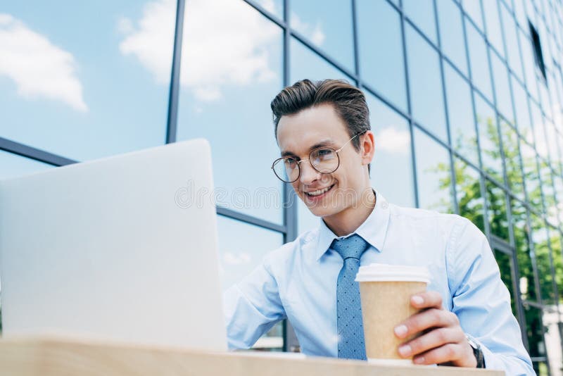 handsome smiling young businessman in eyeglasses using laptop and holding paper cup outside modern royalty free stock images handsome smiling young businessman in eyeglasses using laptop and holding paper cup outside modern royalty free stock images