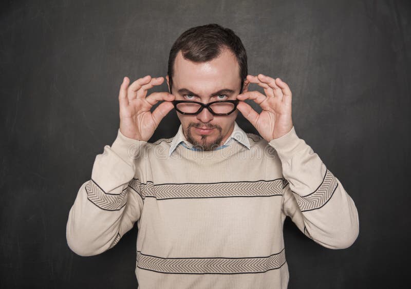 Handsome strict teacher in eyeglasses looking at you on blackboard royalty free stock photography Handsome strict teacher in eyeglasses looking at you on blackboard royalty free stock photography