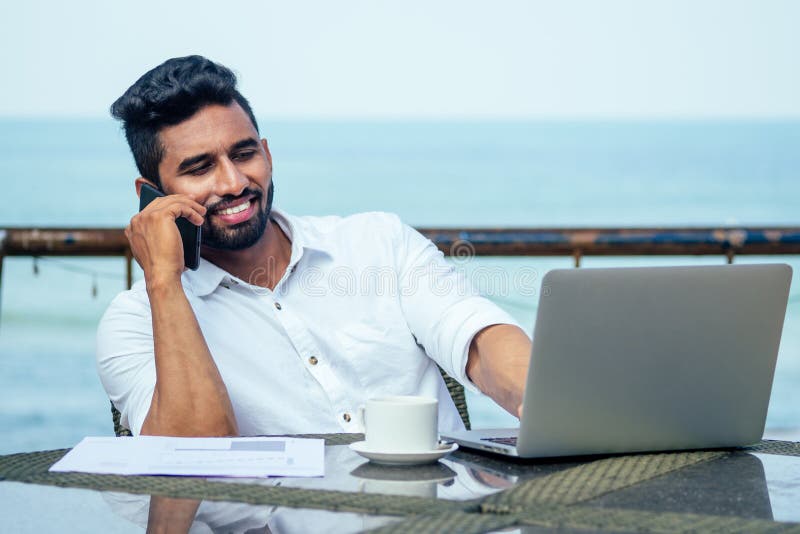 Handsome and successful indian man in a stylish well-dressed freelancer work laptop on the beach.freelance and remote