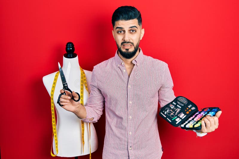 Handsome tailor man with beard holding sew kit and scissors clueless and confused expression royalty free stock photography