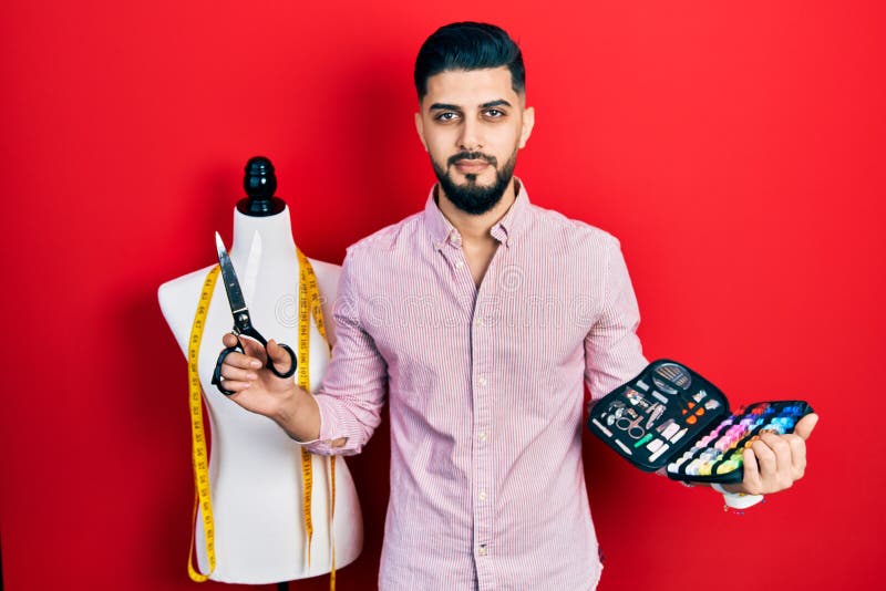 Handsome tailor man with beard holding sew kit and scissors relaxed with serious expression on face royalty free stock photo